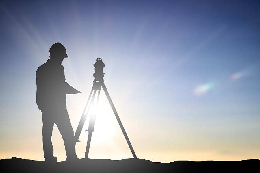 Specialized Business Insurance - Land Surveyer Stands in Silhouette against a Blue Sky with the Sun Shining